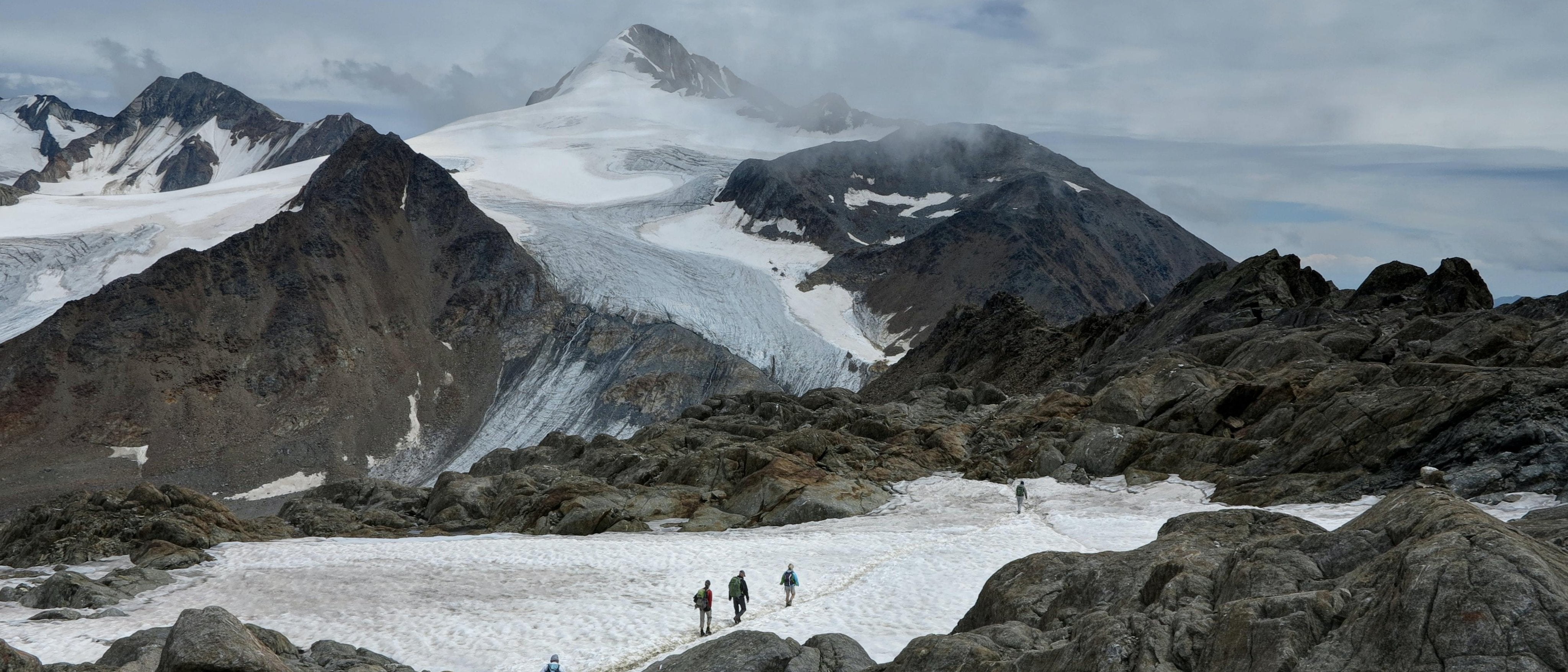 Group Walking across Snow patch in Mountains